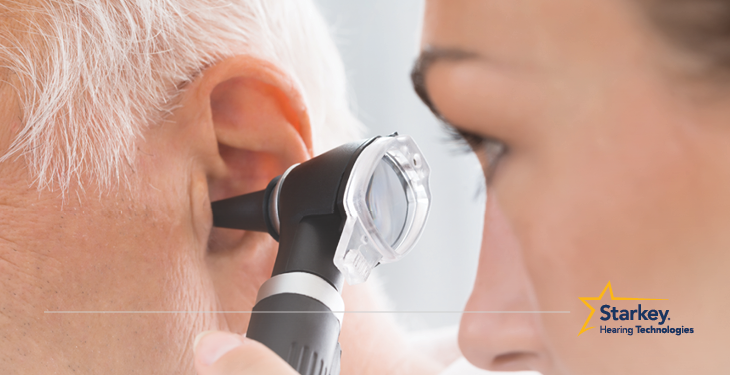 Female doctor looking into an otoscope inserted into an older mans left ear
